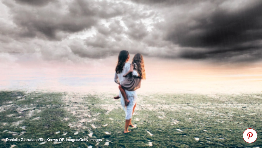 Photo of Mother holding her child while standing in a field.